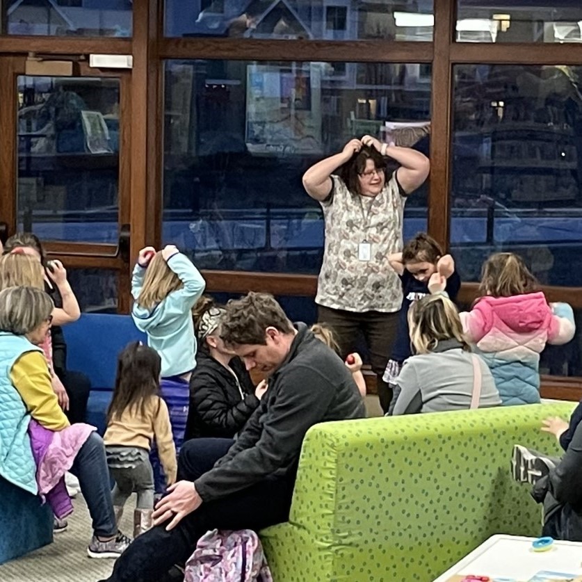 Librarian and children playing together and placing hands on their heads