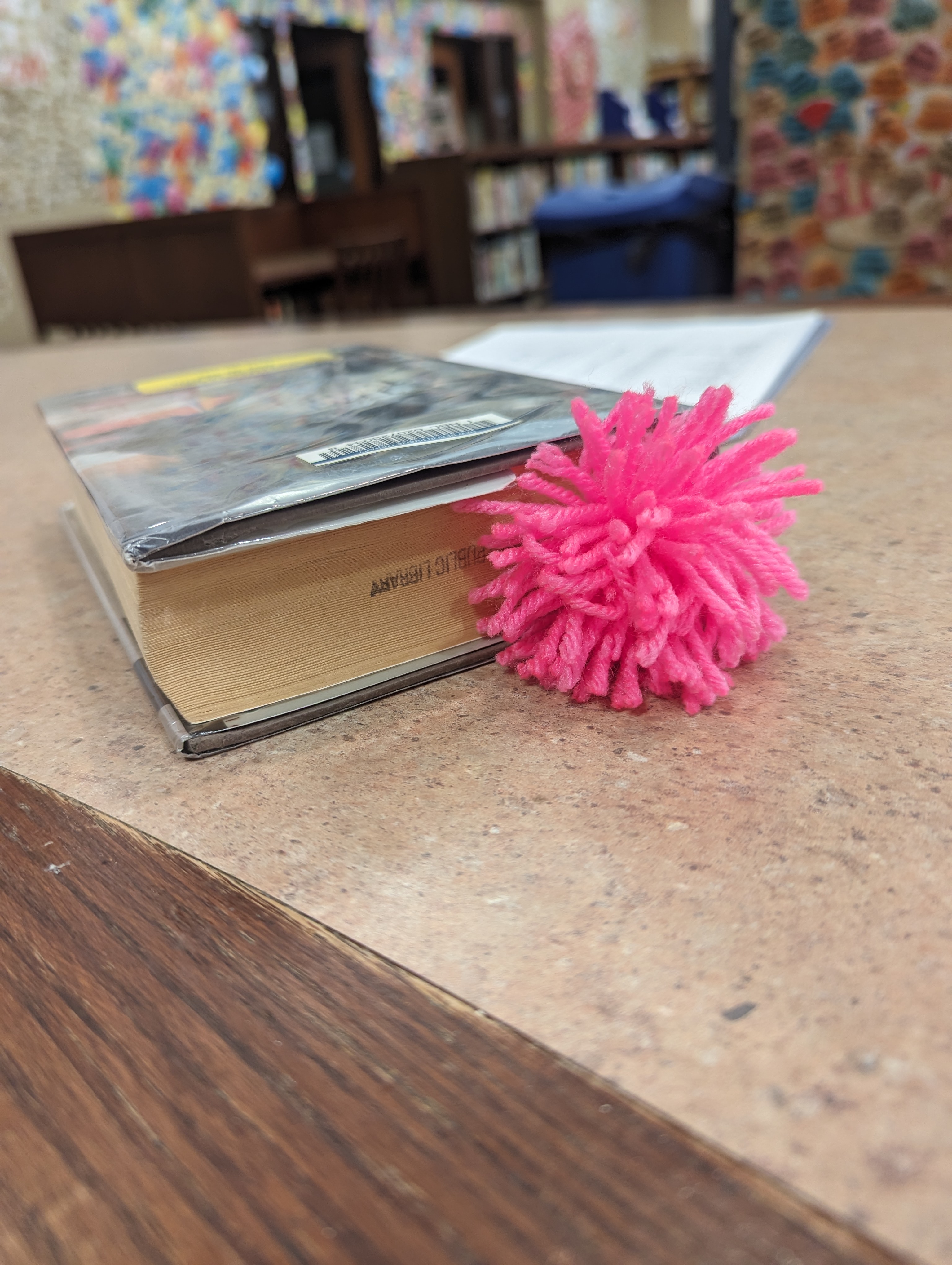 pom pom book mark made out of pink yarn sticking out of a chapter book