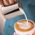 Person pouring cream in a feather design into cup of coffee