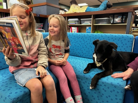 Dog sitting on couch with two children reading a book