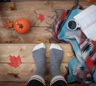 Photo of a person standing in socks next to a book, blanket, coffee, and pumpkin
