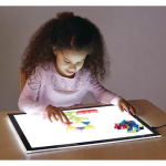 girl with brown curly hair and a pink shirt leaning over a light table with different colored acrylic shapes
