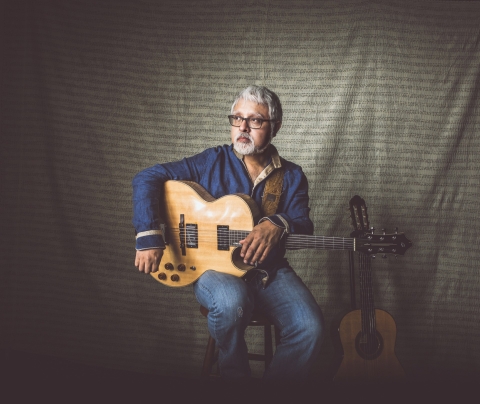 Man positioned on a stool holding an acoustic guitar