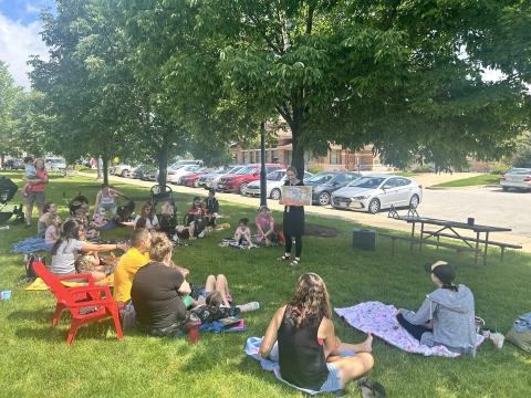 Librarian reading outside with families sitting on grass