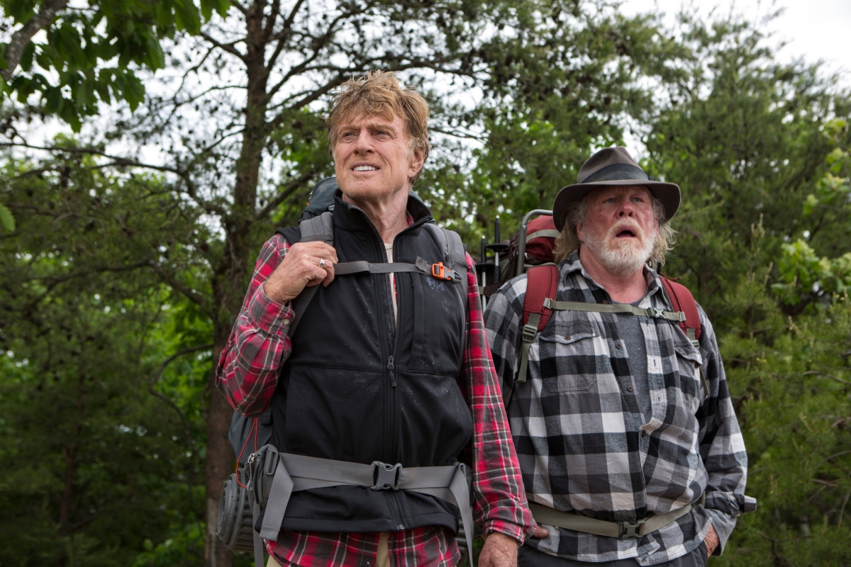 Actors Robert Redford and Nick Nolte in hiking gear in the woods looking off to the distance